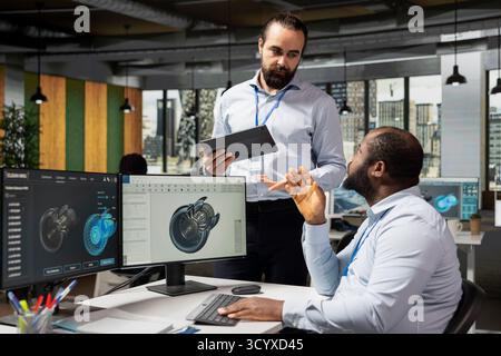 Team of technicians review turbine data on computer to save energy and lower costs. Teamworking colleagues in office using PC to evaluate turbine environmental impact, making adjustments Stock Photo