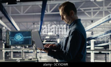 Data center admin on industrial platform checks AI dashboard using laptop. Man in server farm tests artificial intelligence tools on notebook to ensure reliable performance, camera B Stock Photo