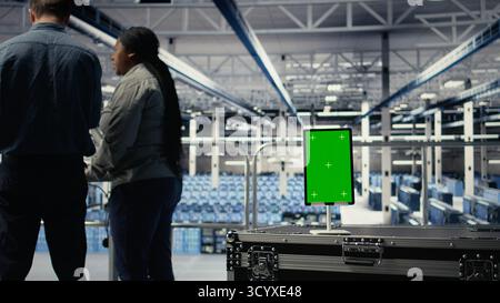 Green screen tablet in server room in front of admins optimizing deep learning systems handling tasks. Mockup device used by data center workers adjusting AI model parameters, camera A Stock Photo