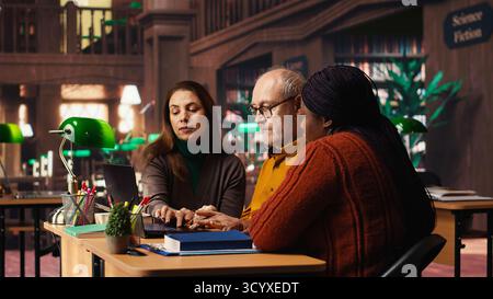 Multiethnic group of students discussing about academic materials, reading and doing research for upcoming exams. Diverse people showing commitment for personal growth. Stock Photo