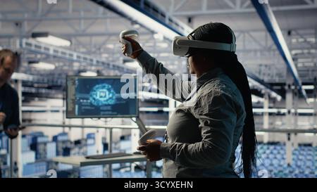 Data center system administrators deploy machine learning software on infrastructure racks. Team of server hub IT experts train AI systems with datasets using tablet to support applications, camera B Stock Photo