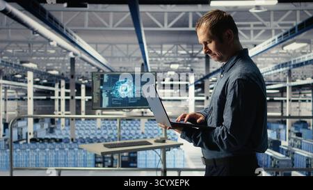 Technician monitors server room activity using laptop while walking through facility. Data center IT professional reviews rigs tests results to ensure systems are working correctly, camera A Stock Photo