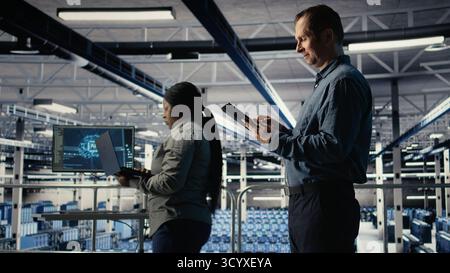 IT expert in server hub uses tablet to optimize deep learning AI systems handling tasks. Data center programmer adjusts artificial intelligence model parameters using device, camera A Stock Photo
