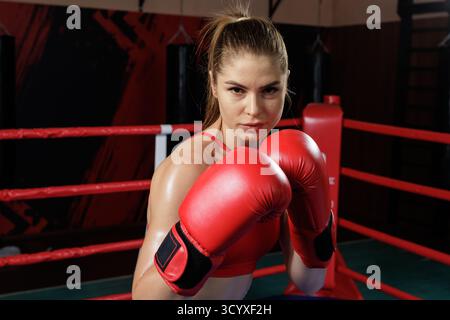 Confident female boxer poses in guard with red gloves in a ring during training, showing focus, strength and determination. Stock Photo