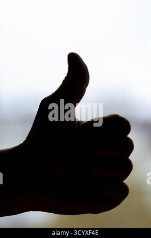 Silhouette Hand Giving Thumbs Up Approval. A dramatic backlit silhouette of a hand showing thumbs up against a bright sky, representing success, motiv Stock Photo