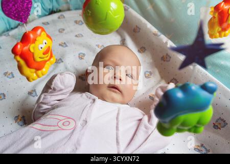Happy baby lying down interacting with hanging toys. People Stock Photo