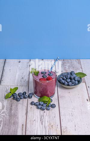 Composition with blueberries and green leaves and a blueberry and pineapple smoothie on a mahogany wood surface Stock Photo
