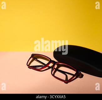 Studio image showing a pair of glasses and a closed black case on a dual-tone yellow and peach surface. The composition has clean shadows and bright t Stock Photo