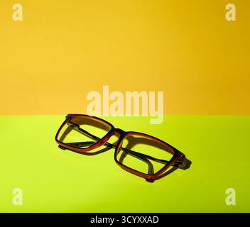 A pair of eyeglasses photographed on a yellow and green background under simulated sunlight. The image has vivid color contrast and clear copy space s Stock Photo