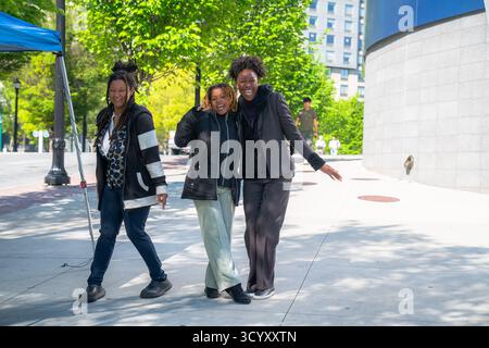 Three women smile and pose for a photo on the sidewalk outside the Georgia Aquarium, surrounded by greenery on a sunny day Stock Photo