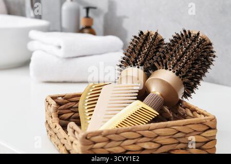 Hair styling. Different combs and brushes in wicker basket on white table in bathroom, closeup Stock Photo