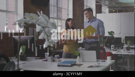 Reviewing office professionals examining yellow document folder in open-plan office, with laptops Stock Photo