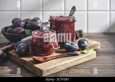 Plum jam in glass jars with ripe plums on a light background Stock Photo