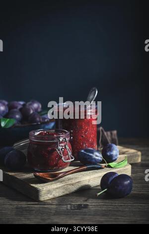 Plum jam in glass jars with ripe plums on a dark background Stock Photo