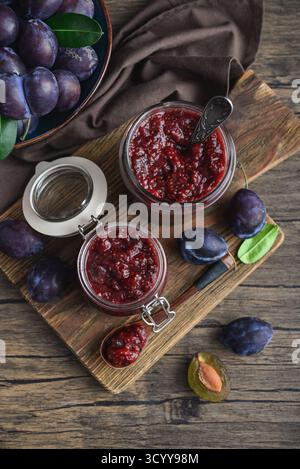Plum jam in glass jars with ripe plums on a wooden background, top view Stock Photo