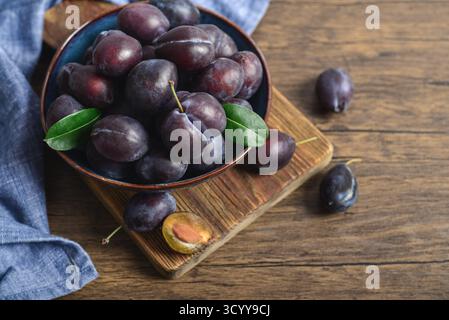 Ripe plums in blue bowl on light background, closeup Stock Photo