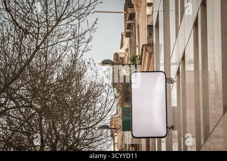 Empty white rectangular sign mounted on a storefront in France. The clean lightbox offers copy space for branding or promotions, hanging beside a city Stock Photo