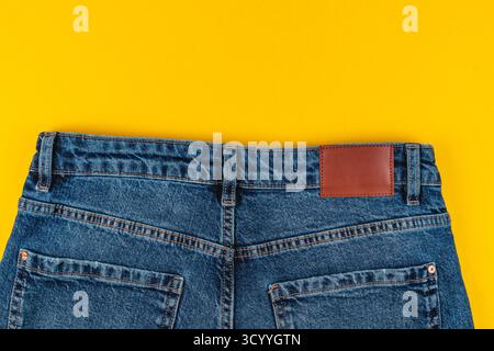 A close-up view of the back of blue denim jeans featuring a brown leather patch. The vibrant yellow background enhances the colors and details of the Stock Photo