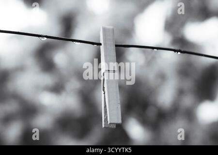 Minimalist black and white photo of a clothespin with raindrops on a wire Stock Photo
