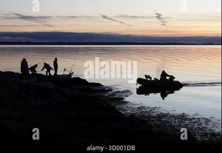 Angler on the beach during sunset, an angler docks on the shore with his inflatable boat and dog, Fehmarn island, 18.10.2025, Fehmarn, Schleswig-Holst Stock Photo
