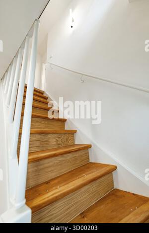 Wooden staircase with white railing and wall lamp in bright, simple staircase, house renovation, climate renovation, Metzingen, Germany Stock Photo