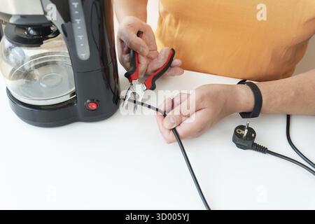 A man is sitting at a table, repairing a small coffee maker with a screwdriver. Close-up Stock Photo