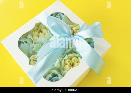 Colorful flower arrangement in a white gift box with a window. A bright blue satin ribbon is tied around the box with an elegant bow Stock Photo