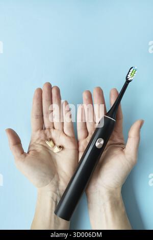 A modern electric toothbrush in one hand and pulled teeth in the other hand on a blue background. Tooth extraction operation. The concept of hygiene f Stock Photo