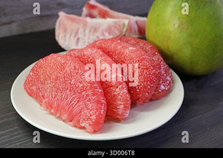 Mouthwatering Peeled Bright Red Pomelo Fruit Segments Lined Up on White Plate Stock Photo
