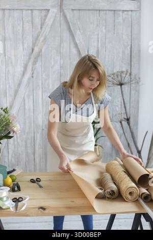 Young florist cutting paper wrapping on table in store for sale of flowers Stock Photo