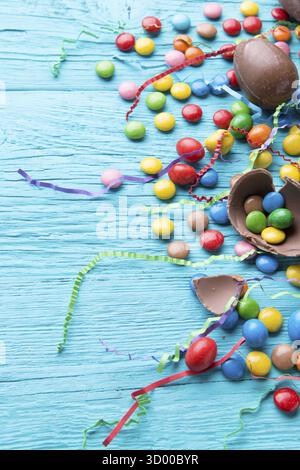 Multicolored dragees, chocolate eggs, ribbons on blue wooden table Stock Photo