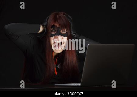 Brunette hacker in black mask screaming at computer Stock Photo
