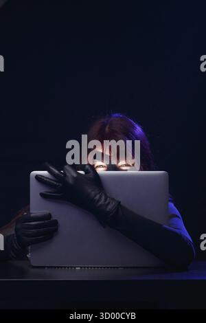 Thief in mask holds laptop in hands at night Stock Photo