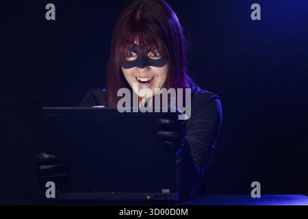 Thief woman in black mask next to computer Stock Photo