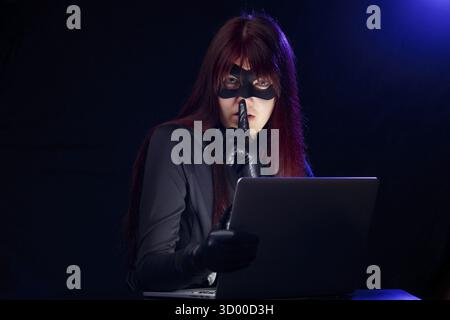 Brunette hacker with finger at mouth near laptop Stock Photo