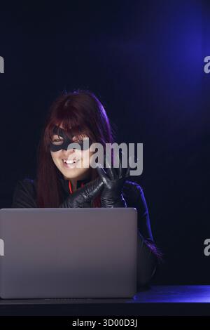Brunette thief in black mask hacking computer Stock Photo