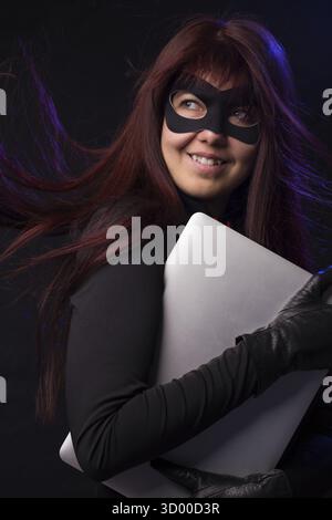 Thief with long hair in mask holds laptop Stock Photo