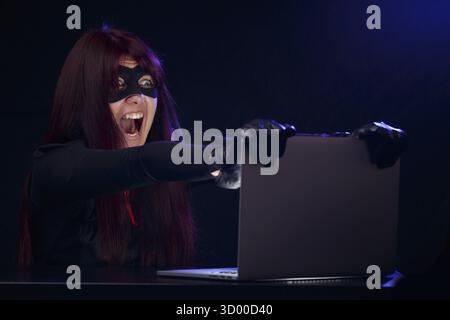 Thief in black mask at night near computer Stock Photo