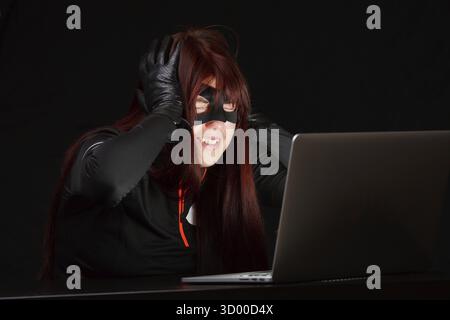 Happy hacker in black mask next to computer Stock Photo