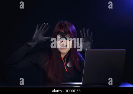 Brunette hacker in black mask with raised hands in gloves Stock Photo
