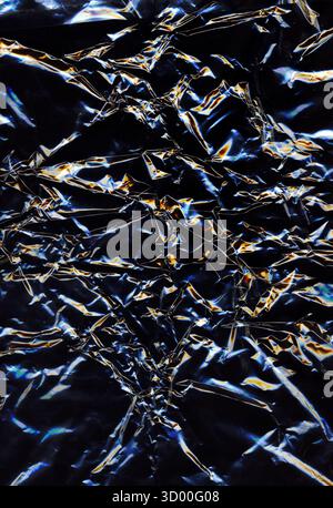 Abstract dark crumpled plastic texture with glowing light reflections creating a metallic and futuristic effect. Shiny surface and intricate folds for Stock Photo