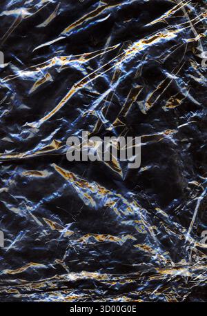 Abstract dark crumpled plastic texture with glowing light reflections creating a metallic and futuristic effect. Shiny surface and intricate folds for Stock Photo