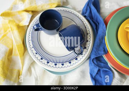 A pyramid of brightly colored bowls, plates and cups of different sizes and colors on the kitchen table. Scandinavian style, minimalism. View from abo Stock Photo