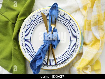 Gold cutlery is tied with a blue napkin, on which the plates are on a green-yellow linen napkin. Minimalist design, rustic. Birthday or wedding celebr Stock Photo