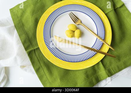 Easter serving concept. Festive table setting with bright napkins and yellow-blue plates with dishes and decorated eggs Stock Photo