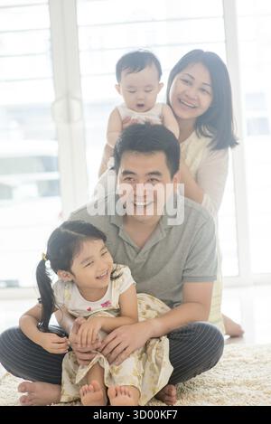 Chinese parents and children piggy back. Happy Asian family spending quality time at home, natural living lifestyle indoors Stock Photo