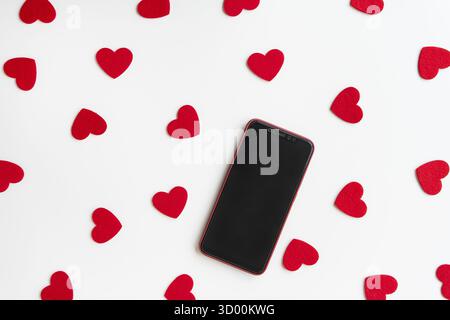 Smartphone surrounded by red felt hearts on a white background. Place for an inscription Stock Photo
