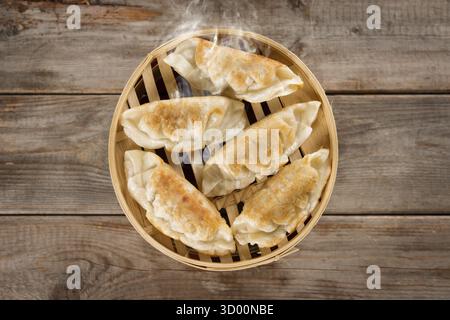 Top view fresh pan fried dumpling on bamboo basket. Chinese food with hot steams on rustic vintage wooden background Stock Photo
