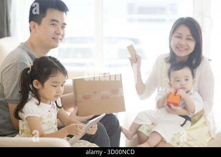 Online shopping using digital tablet pc and payment with credit card. Happy Asian family at home, natural living lifestyle indoors Stock Photo