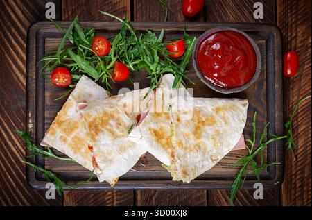 Traditional mexican quesadillas with sliced ham also called sincronizadas on wooden background. Overhead Stock Photo